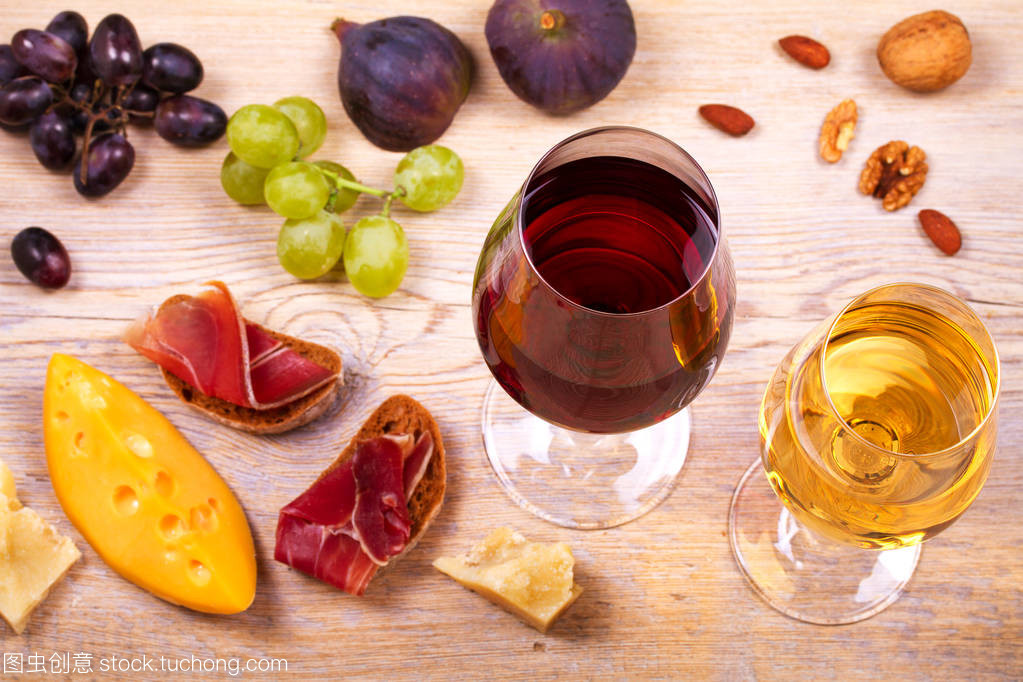 紅色和白色奶酪、 火腿、 無花果和葡萄與葡萄酒杯。木制的桌子上的酒杯。葡萄酒的靜物
